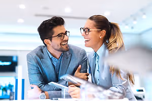 A smiling couple in a suit wearing eyeglasses sitting at a table in a business room