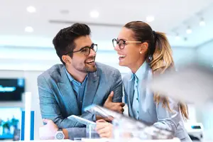 A smiling couple in a suit wearing eyeglasses sitting at a table in a business room