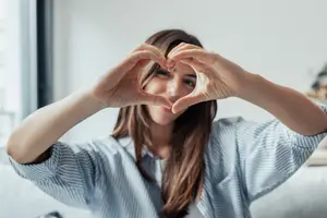 Woman forming a heart shape with her hands in a room