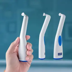 A hand holding a white and blue toothbrush with three toothbrushes in the background