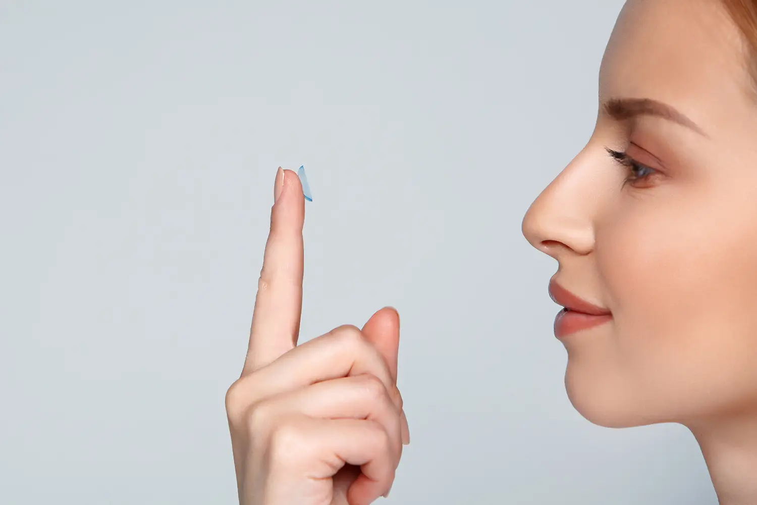 A woman holding a blue contact lens with her finger
