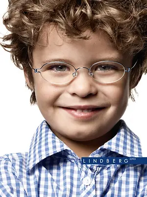 A young boy with curly hair wearing glasses and a blue checkered shirt is smiling and looking at the camera with the brand name Lindberg visible in the bottom right corner of the image.