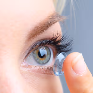 Close up of a woman putting a contact lens into her eye.