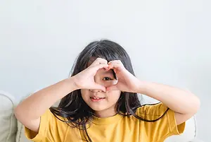 Little girl wearing yellow shirt making heart shape with her hands
