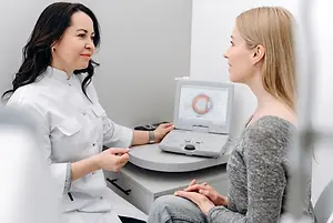 A doctor examines a patient's eyes with a medical device in an office.