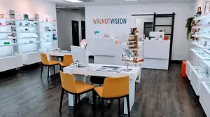 Walnut Vision optical store interior with yellow chairs and white furniture, a monitor, and a mirror.