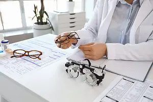 A woman in a lab coat is examining a pair of glasses in a laboratory setting.