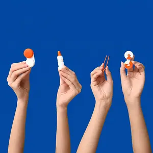 Four hands hold eye care products on a blue background