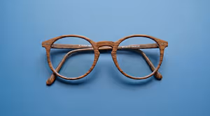 A pair of glasses with wooden frames and clear lenses are displayed on a blue background.