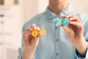 Close up of a man holding a pair of eye drops in one hand and a pair of lenses in the other hand