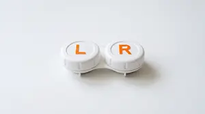 Two white lenses for contact lenses with the letters L and R on them are placed on a white surface