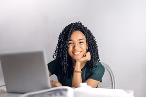 Woman sitting at desk with laptop and books smiling at camera