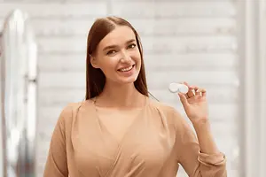 Woman holding up a pair of white colored contact lenses