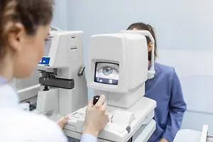 A woman is examining another woman's eye with a machine in an eye clinic