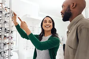 A woman pointing to glasses on a rack while a man looks on