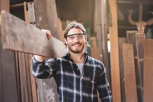 man in glasses and plaid shirt holding a piece of wood