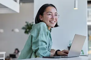 Asian woman in eyeglasses using a laptop in a modern office