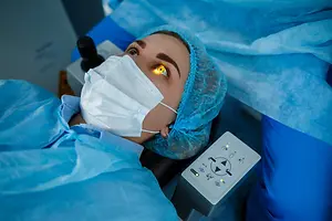 Woman in surgical attire wearing a face mask and eye protection with a laser light illuminating her eye