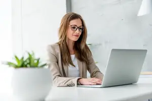 A woman is sitting in front of a desk and is working on her laptop computer.