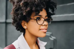 A woman with curly hair and glasses is looking sideways
