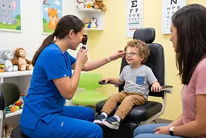 A child is getting an eye exam from a woman in a blue shirt in a pediatric optometrist's office.