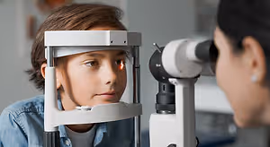 A young boy undergoing an eye exam by a woman in a clinic.
