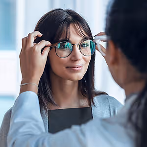 A woman with glasses on and a doctor holding them up to her face looking at her