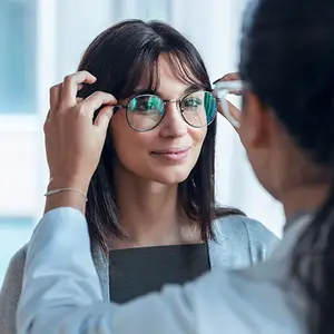 A woman with glasses on and a doctor holding them up to her face looking at her