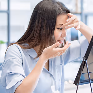 A woman is looking at her contact lens in her hand.