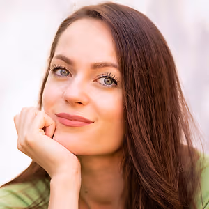 A smiling woman with brown hair and pink lipstick is posing for a photo.