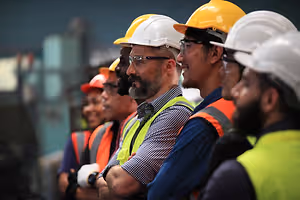 Workers in safety gear stand in a line inside a factory.