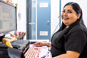 A woman sitting at a desk wearing a headset smiling for the camera