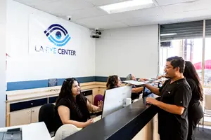 Inside the LA Eye Center, two women are sitting while a man stands at the front desk, holding a paper and looking at them.