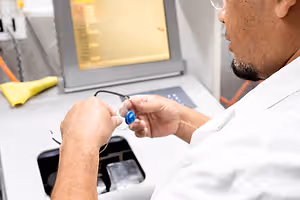 A medical technician is working with a medical device and examining a blue object with a wire