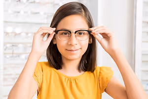 A girl in a yellow blouse is trying on glasses in a store