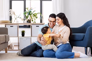 A family sitting on the floor with a baby, smiling and looking at the camera