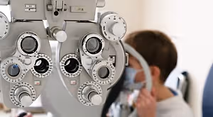 A young boy is examining his eyes with a slit lamp in a medical clinic.