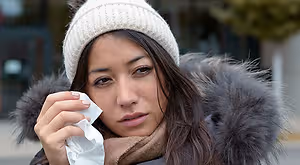 A woman with a scarf and a hat wiping her nose with a tissue