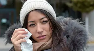 A woman with a scarf and a hat wiping her nose with a tissue