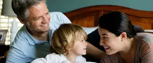 A man and a woman are smiling with a child in bed behind them