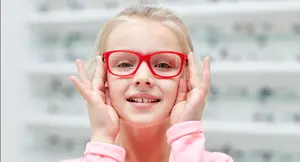 A young girl with red glasses smiling inside a shop