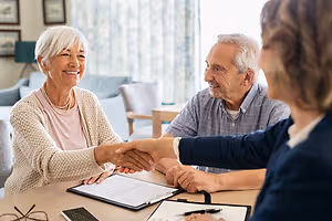 A woman shakes hands with a man and a woman in a living room
