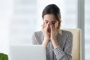 woman sitting at desk covering face with hands looking tired and stressed