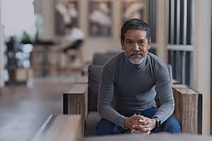 A man sitting in a chair in a room with a gray shirt and blue pants