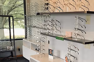 An optical shop with shelves of glasses, cabinets, a window, and a picture of a person in the middle