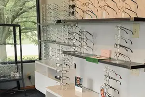 An optical shop with shelves of glasses, cabinets, a window, and a picture of a person in the middle