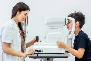 A woman is adjusting a device for a boy who is looking at it inside a clinic