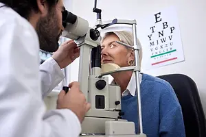 An older woman having her eye examined by an optometrist using an ophthalmoscope