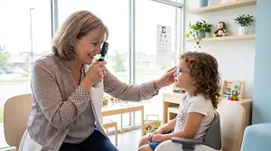 An adult woman is examining a child's eye with an ophthalmoscope.