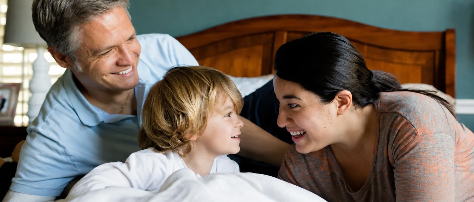 Smiling parents cuddling with their young child in bed